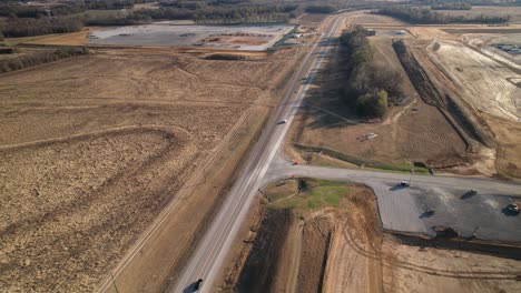 Aerial-following-cars-travelling-down-highway-adjacent-to-sprawling-new-construction