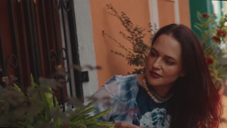 Beautiful-Indian-model-sitting-down-and-looking-at-the-plants-around-her,-in-the-streets-of-the-colorful-town-of-Fontainhas,-India