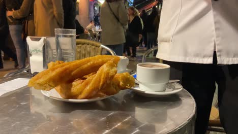 Primer-Plano-De-Un-Camarero-Que-Sirve-Porras-Y-Chocolate-Caliente-En-La-Calle-De-Un-Bar-Típico-En-Madrid,-España