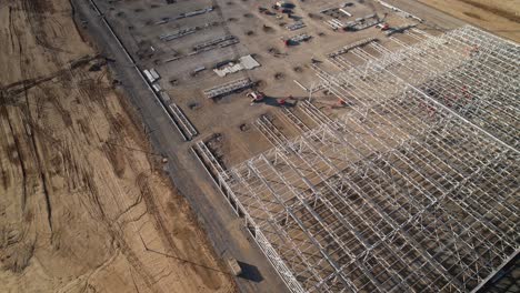 Aerial-zoom-out-of-steel-structure-under-construction-surrounded-by-heavy-machinery-and-cranes