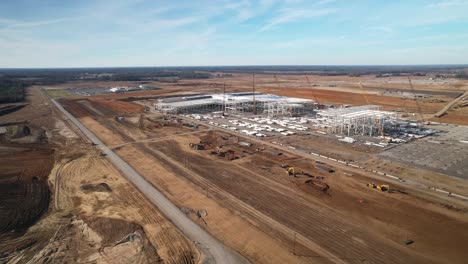 Ascenso-Aéreo-Y-Aproximación-A-Una-Gran-Estructura-De-Acero-En-Construcción-Rodeada-De-Grúas,-Equipo-De-Construcción-Y-Tierra-Nivelada