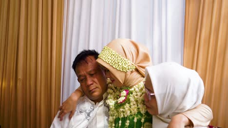 The-bride-is-in-the-laps-of-her-father-and-mother,-they-kiss-each-other-on-the-cheek-and-cry-sadly-at-the-traditional-Javanese-"siraman"-event