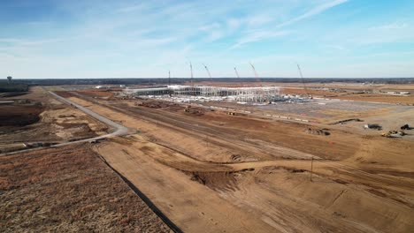 Panorámica-Lenta-Aérea,-Alrededor-De-Una-Gran-Estructura-De-Acero-En-Construcción-Rodeada-De-Grúas,-Equipo-De-Construcción-Y-Tierra-Graduada