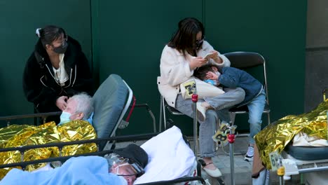 Una-Madre-Y-Su-Hijo-Esperan-Para-Ser-Tratados-Después-De-Mostrar-Síntomas-De-Covid-19-Mientras-Los-Pacientes-Enfermos-Descansan-Y-Se-Acuestan-En-Camas-Fuera-De-Un-Hospital-Abarrotado-Mientras-El-Sistema-Médico-Colapsa-Con-Las-Hospitalizaciones