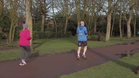 Active-fitness-group-jogging---walking-in-wet-rainy-park-in-slow-motion-tracking-right-slow