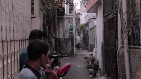 Hombres-Del-Sudeste-Asiático-Sentados-En-Un-Callejón-Y-Un-Hombre-Que-Lleva-Un-Gran-Saco-De-Golosinas-Usando-Una-Moto,-En-Algún-Lugar-De-Yakarta