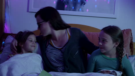 Mom-tucks-her-two-little-girls-into-bed-with-a-kiss-on-the-head