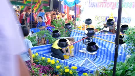 Niño-Asiático-Arrojando-Monedas-A-Ollas-Giratorias-En-Un-Evento-Festivo