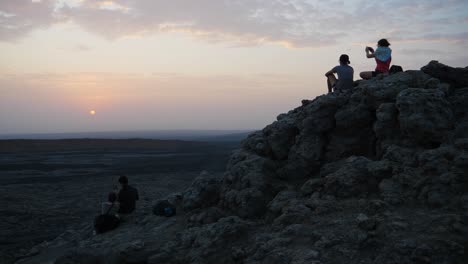 Daueraufnahme-Von-Menschen,-Die-Auf-Einer-Felsformation-Sitzen-Und-Den-Sonnenaufgang-Beobachten