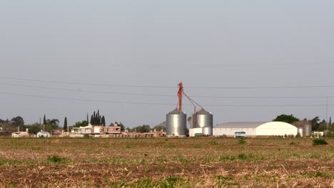 Silos-Y-Un-Almacén-En-El-Fondo-De-Un-Campo-Cubierto-De-Rastrojos