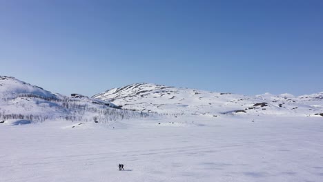 Vista-Aérea-De-Personas-Esquiando-Sobre-Un-Lago-Congelado-En-Un-Paisaje-Montañoso-Nevado