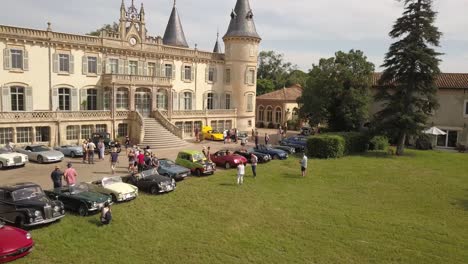 Vista-Aérea-De-Drones-De-Una-Exposición-De-Autos-Antiguos-Frente-A-Un-Castillo