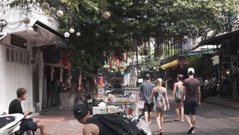 Group-of-friends---travelers-walking-in-Bangkok-urban-area-while-local-Thais-are-cleaning-the-road-from-the-night-before----locals-looking-at-tourists----stabilized-full-HD-shot