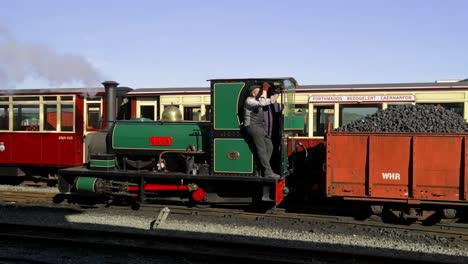 Ferrocarril-Ffestiniog:-El-Ingeniero-Desvía-La-Máquina-De-Vapor-De-Vía-Estrecha-Lilla-Hacia-Atrás-Con-Camiones-Llenos-De-Carbón,-Estación-De-Tren-Del-Puerto-De-Porthmadog,-Snowdonia,-Gales:-Hombre-Con-Gorra,-Slomo-60fps