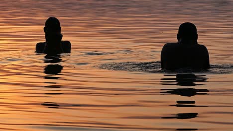 Beautiful-cinematic-shot-of-people-taking-dip-in-holy-river-ganga-in-Varanasi-during-sunrise-time-making-the-water-shine-all-gold