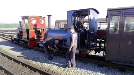 Ferrocarril-Ffestiniog---Dos-Ingenieros-Preparan-El-Motor-De-Vapor-De-Vía-Estrecha-Britomart-Para-La-Salida-En-La-Estación-De-Tren-Del-Puerto-De-Porthmadog,-Snowdonia,-Gales---Hombre-Calvo,-Hombre-Con-Gorra,-Slomo-60fps