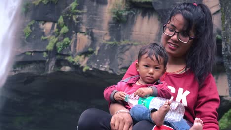 Mother-holding-her-cute-kid-during-their-visit-to-jogini-waterfall,-manali