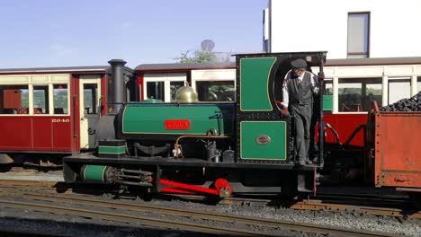 Ferrocarril-Ffestiniog:-El-Ingeniero-Desvía-El-Motor-De-Vapor-De-Vía-Estrecha-Lilla-Hacia-Adelante-Con-Camiones-Llenos-De-Carbón,-Estación-De-Tren-Del-Puerto-De-Porthmadog,-Snowdonia,-Gales:-Hombre-Con-Gorra,-Slomo-60fps