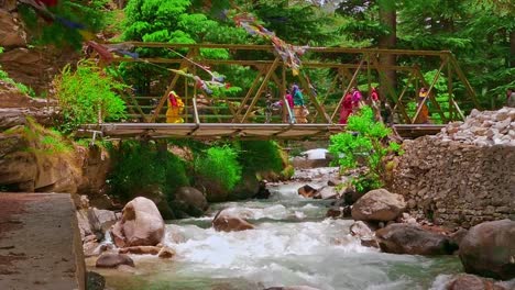 Toma-Cinematográfica-En-Cámara-Lenta-De-Personas-Que-Cruzan-El-Puente-Sobre-El-Agua-Cristalina-Del-Río-Ganges-Que-Fluye-Río-Abajo-Desde-Las-Montañas-En-El-Pueblo-De-Uttarakhand-De-Roughal