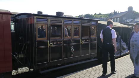 Kutschen-Von-Touristen-Und-Touristen-Fahren-In-Porthmadog-Harbour-Railway-Station,-Ffestiniog-Railway-Ein,-Während-Wachmann-Und-Ingenieur-Auf-Dem-Bahnsteig-Die-Wege-Kreuzen,-Ingenieur-Hält-Inne,-Um-Zu-Bewundern,-Slomo-60fps