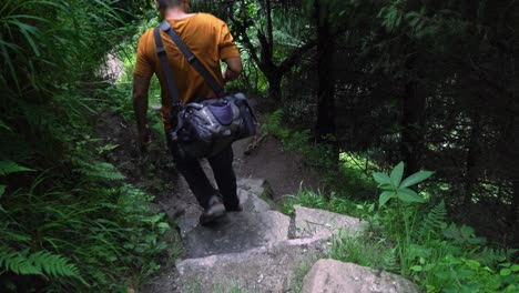 Following-shot-of-a-man-trekking-down-from-jogini-waterfalls-in-himalayan-region