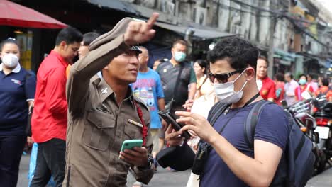 Hombre-Asiático-Con-Mascarilla-Pidiendo-Direcciones-Al-Oficial-De-Policía