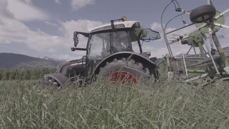 Tractor-working-on-alpine-meadow,-mowing-fresh-lush-grass-for-fodder