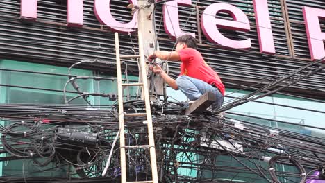 Joven-Asiático-Arreglando-Un-Cable-Al-Otro-Lado-De-La-Calle,-Baja-La-Escalera