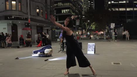 Hermosa-Mujer-Joven-Descalza-De-Piel-Oscura-Con-Cabello-Largo-Y-Suelto-Bailando-En-La-Calle-De-La-Ciudad-Por-La-Noche-Mientras-El-Músico-Callejero-Toca-La-Guitarra---4k,-59