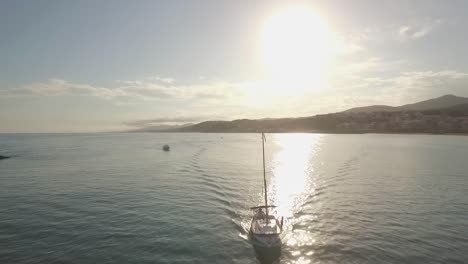 Little-sailing-boat-with-two-people-onboard-entering-the-port-of-Arenys-de-Mar-at-evening,-orbiting-aerial-shot