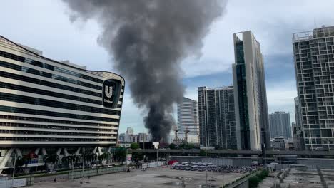 Espeso-Humo-Negro-Que-Se-Eleva-Hacia-El-Cielo-Desde-Un-Edificio-En-Llamas-En-Rama-Ix-Road,-Huang-Khwai,-Bangkok,-Tailandia-Cerca-Del-Edificio-De-La-Casa-Unilever-Durante-El-Día---Toma-Amplia