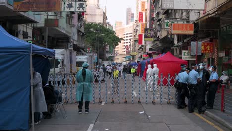 Health-workers-dressed-in-PEE-suits-and-police-officers-stand-guard-in-front-of-a-barrier-in-an-area-under-lockdown-to-contain-the-spread-of-the-Coronavirus-variant-outbreak-in-Hong-Kong