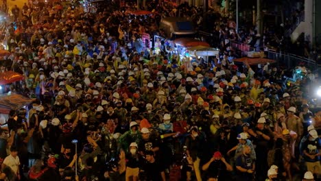 Demonstranten-Mit-Schutzhelmen-Marschieren-Nachts-Auf-Der-Straße-In-Bangkok,-Thailand---High-Angle-Shot