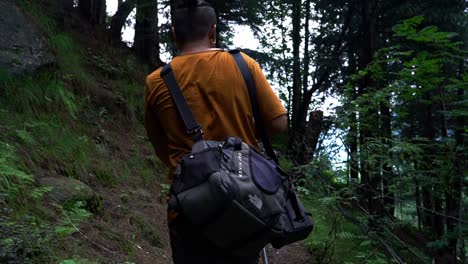 Vista-Detrás-De-Un-Excursionista-Masculino-Con-Bolsas-Caminando-Por-El-Sendero-Del-Bosque-En-La-Montaña---Cámara-Lenta