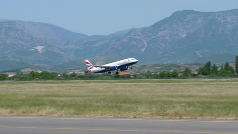 Toma-De-Seguimiento-De-Un-Avión-Airbus-A320-De-British-Airways-Despegando-Con-Montañas-En-El-Fondo