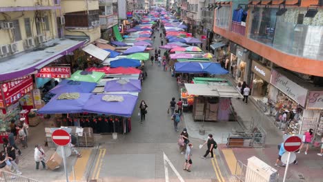 A-wide-high-view-shot-of-shoppers-walking-through-the-Fa-Yuen-street-outdoor-market-stalls-selling-vegetables,-fruits,-gifts,-and-fashion-goods-in-Hong-Kong