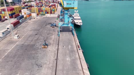 Vista-Aérea-De-Una-Mujer-Que-Camina-Hacia-Una-Gran-Grúa-Azul-En-Un-Puerto-De-Carga-Cercano,-Tira-Hacia-Atrás