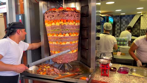 Hombre-Cortando-Carne-De-Un-Asador-Vertical-En-Un-Restaurante-De-Kebab-En-Bodrum-Turquía,-Gente-Trabajando-En-La-Cocina,-Deliciosa-Comida-Tradicional,-Carne-Sazonada-Con-Patatas-Y-Zanahorias,-Tiro-De-4k