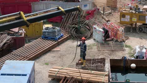 Un-Trabajador-De-Ingeniería-Chino-Ayuda-A-Una-Grúa-A-Tirar-De-Una-Pila-De-Tablas-De-Madera-En-Un-Proyecto-De-Construcción-En-Desarrollo-En-Hong-Kong