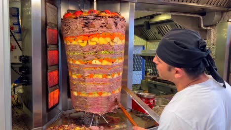 Hombre-Cortando-Carne-De-Un-Asador-Vertical-En-Un-Restaurante-De-Kebab-En-Bodrum-Turquía,-Gente-Trabajando-En-La-Cocina,-Sabrosa-Comida-Tradicional,-Carne-Sazonada-Con-Patatas-Y-Zanahorias-En-Un-Palo,-Tiro-De-4k