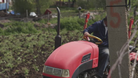 Ein-Geschickter-älterer-Landwirt-Manövriert-Einen-Kleinen-Roten-Traktor-Rückwärts,-Während-Er-An-Einem-Sonnigen-Tag-Im-Dorf-Moliti,-Georgia,-Das-Feld-Pflügt