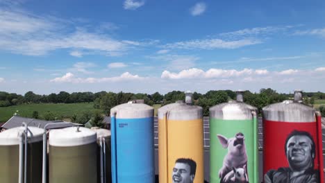 Acercamiento-Aéreo-Bajo-Del-Dibujo-De-La-Decoración-De-Graffiti-De-La-Familia-De-Agricultores-Con-Animales-En-Grandes-Contenedores-De-Silo-De-Existencias-Agrícolas-Que-Revelan-Un-Entorno-Agrícola-Más-Amplio