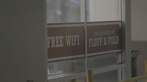 Video-Vom-Tor-Des-Waschsalons-Fluff-And-Fold-Mit-Einem-Schild,-Auf-Dem-Steht,-Dass-Es-Im-Waschsalon-In-Los-Angeles-Kostenloses-Wlan-Sowie-Eine-Abhol--Und-Rückgabemöglichkeit-Gibt