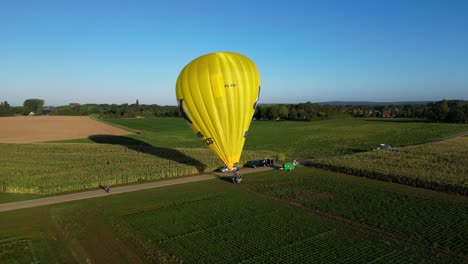 Aerial-Morning-View-Of-Bright-Yellow-Hot-Air-Balloon-Being-Prepared-For-Flight-In-Field-In-The-Netherlands