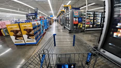 Punto-De-Vista-Mientras-Empuja-Un-Carrito-Hacia-La-Sección-De-Congelados-De-Walmart-Desde-El-Pasillo-Principal-Donde-Se-Ven-Las-Galletas-Y-La-Ropa