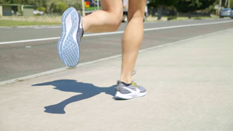 Cierra-Las-Piernas-De-La-Atleta-Femenina-Con-Zapatillas-Para-Correr-A-Lo-Largo-De-La-Acera-Suburbana,-4k