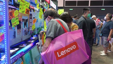 Un-Comprador-Chino-Sostiene-Una-Bolsa-De-Compras-De-Lenovo-Mientras-Busca-Televisores-Exhibidos-En-El-Festival-De-Computadoras-Y-Comunicaciones-De-Hong-Kong-Mientras-La-Gente-Compra-Productos-Electrónicos-Con-Descuento