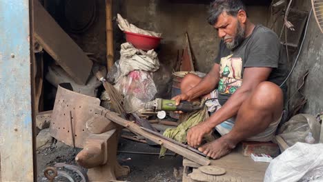 Close-up-shot-of-man-sharpening-and-shaping-a-sword-blade-by-wielding-in-a-workshop-it-at-daytime