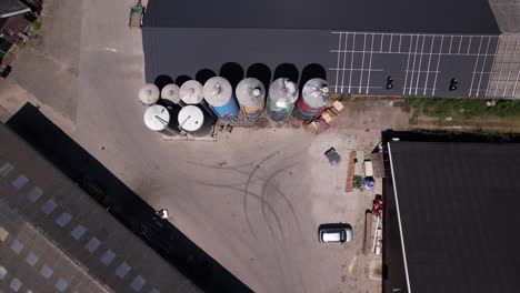 Aerial-top-down-descending-movement-showing-decoration-drawing-of-farmers-family-with-animals-on-large-farm-stock-silo-containers-contrasted