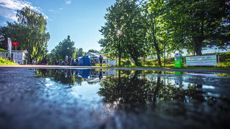 Low-angle-shot-from-camera-placed-beside-a-puddle-on-the-road-of-spectators-entering-the-stadium-in-timelapse-in-Riga,-Latvia-at-daytime